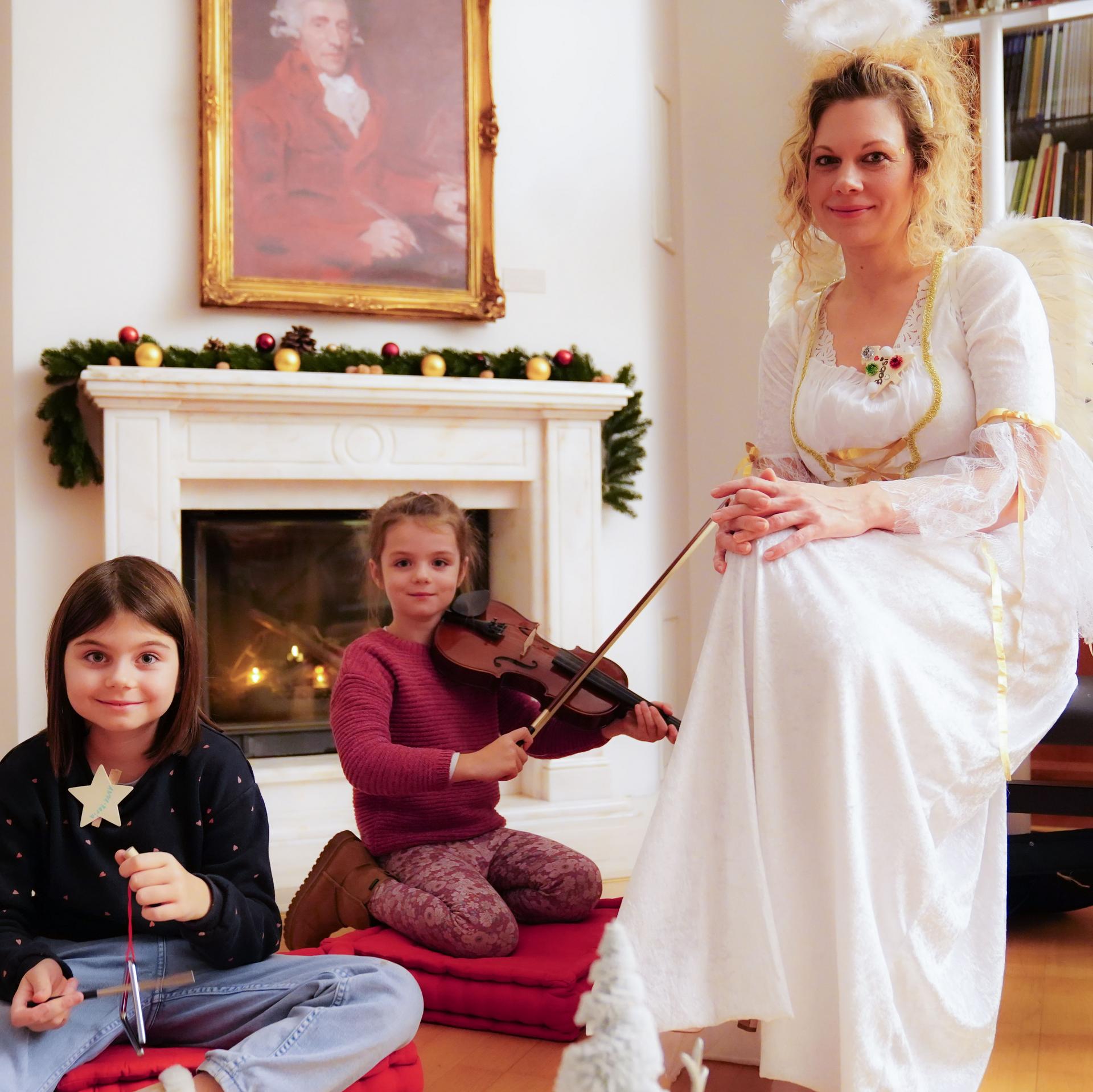 Zwei Kinder sitzen vor dem weihnachtlich geschmückten Kamin im Haydn-Haus daneben eine Frau als Christkind verkleidet