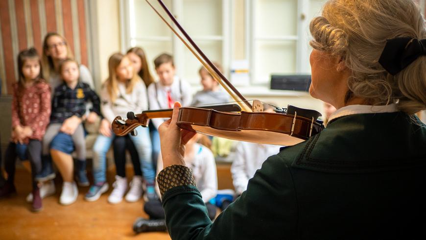 Geigenspieler:in vor einer Kindergruppe
